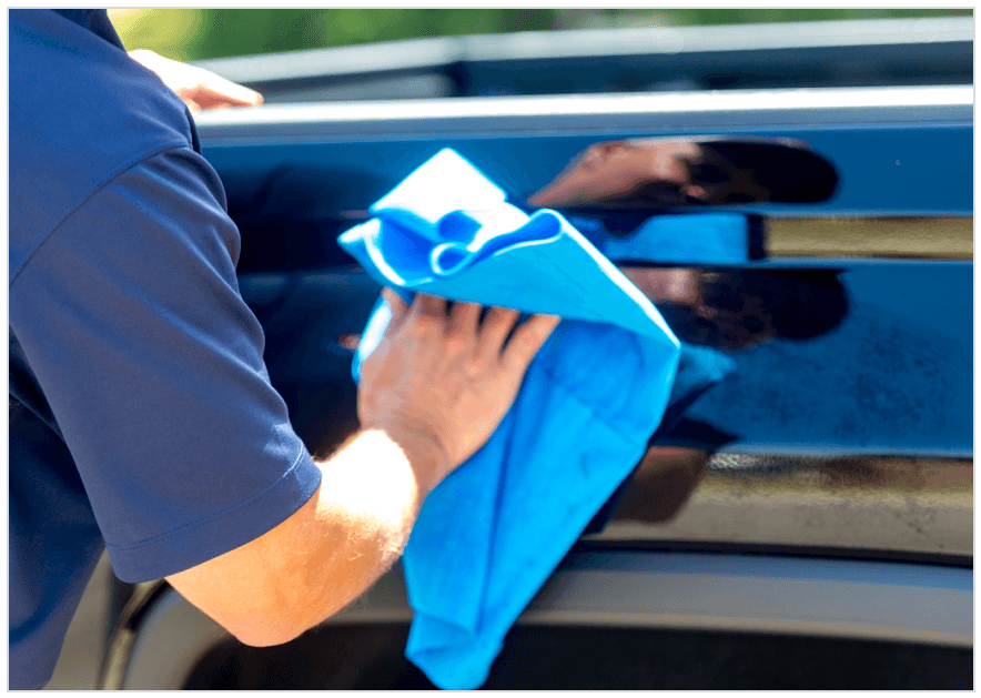 A blue colored shirt person whipping the car with the cloth